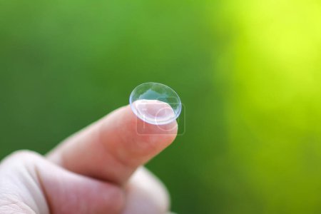 Photo for "Transparent contact lens on finger tip on blurred green summer nature background" - Royalty Free Image