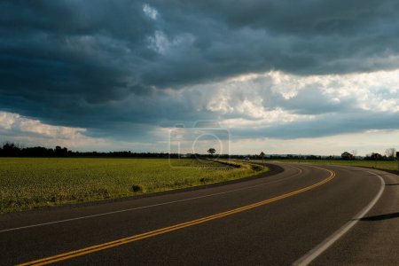 Téléchargez les photos : "Route courbe avec nuages orageux estivaux spectaculaires" - en image libre de droit