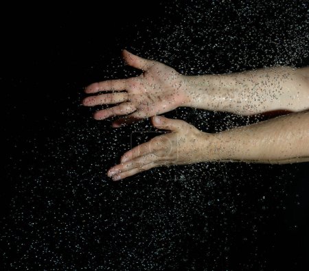 Téléchargez les photos : "deux mains féminines et des gouttes d'eau volantes sur un fond noir" - en image libre de droit