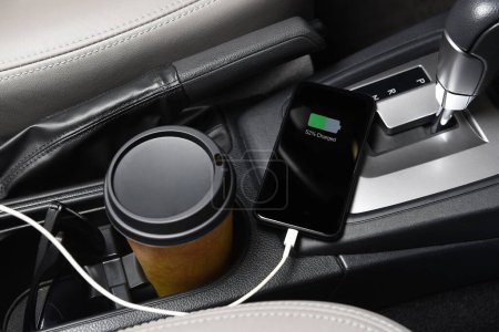Photo for A SmartPhone plugged in the charging port on the console of a modern automobile, closeup with coffee cup and sunglasses" - Royalty Free Image