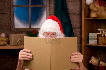 Photo for Santa Claus in Workshop With Large Book - Royalty Free Image