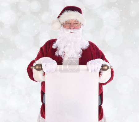 Photo for Santa Claus holding a scroll of paper in front of his body, over a bokeh background with snow effect. The paper is blank with room for your copy - Royalty Free Image