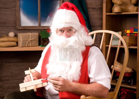 Foto de Santa Claus pintando avión de juguete en su taller - Imagen libre de derechos