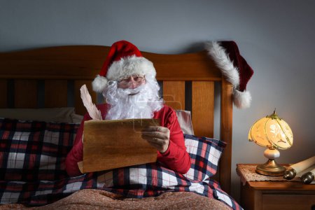 Photo for Santa Claus sitting up in his bed working on his naughty and nice list. - Royalty Free Image