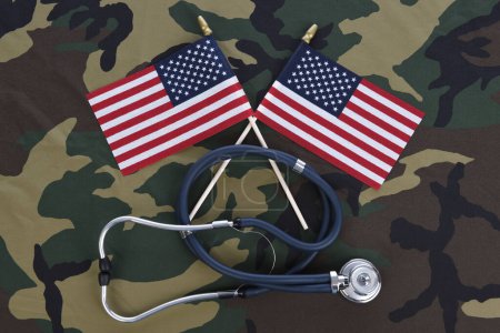 Photo for "Military Health Care Concept. Camouflage background with stethoscope and two crossed American flags." - Royalty Free Image