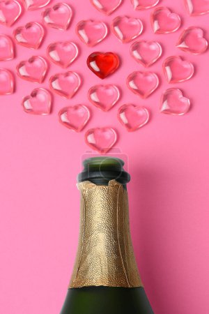 Foto de Concepto del Día de San Valentín: plano de ángulo alto de una botella de champán blanco con corazones de cristal rosa simulando un spray
. - Imagen libre de derechos