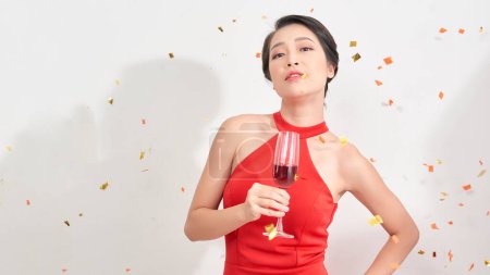 Foto de "Hermosa chica asiática en vestido de noche sonriendo, sosteniendo copa de champán sobre fondo blanco." - Imagen libre de derechos