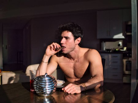 Téléchargez les photos : "attrayant chemise jeune homme manger petit déjeuner à la maison" - en image libre de droit