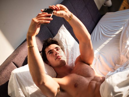 Téléchargez les photos : "Jeune homme attrayant utilisant un téléphone portable pour prendre des photos selfie" - en image libre de droit