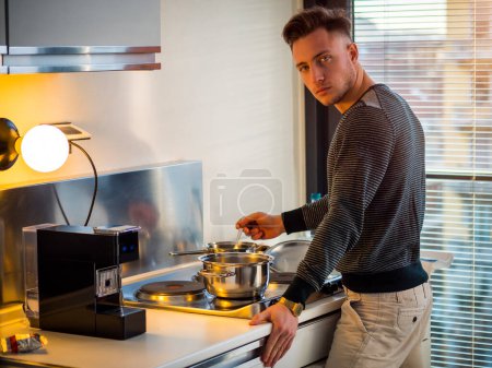 Photo for "Young man in kitchen at home, cooking at the stove" - Royalty Free Image