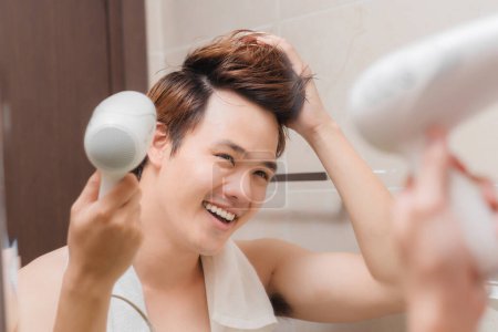 Foto de "Joven de moda secándose el pelo con secador de pelo delante del espejo del baño
" - Imagen libre de derechos