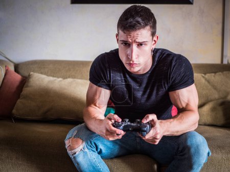 Foto de "Atractivo chico jugando videojuegos con joystick en la mano" - Imagen libre de derechos