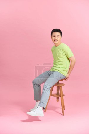Foto de Eager smart casual man looking away sitting on a stool on pink studio background - Imagen libre de derechos