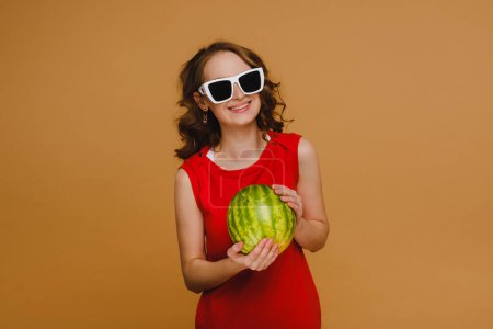 Photo for A beautiful girl in glasses and a red dress holds a watermelon in her hands - Royalty Free Image