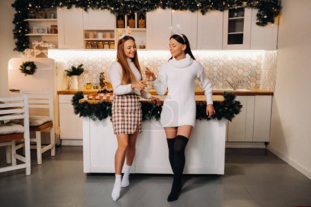 Foto de Dos chicas en un ambiente acogedor en casa con champán en sus manos en Navidad. Las chicas sonrientes beben champán en una velada festiva - Imagen libre de derechos