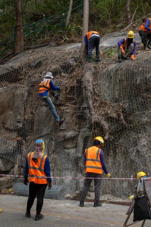 Téléchargez les photos : "Les travailleurs de la construction utilisent le maillage pour couvrir les grandes roches sur le côté de la route. Afin de ne pas laisser tomber la pierre." - en image libre de droit