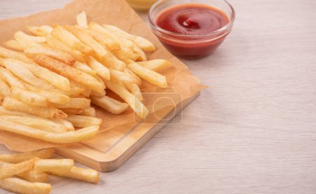 Téléchargez les photos : Golden yummy deep French fries on kraft baking sheet paper and serving tray to eat with ketchup and yellow mustard, top view, lifestyle. - en image libre de droit