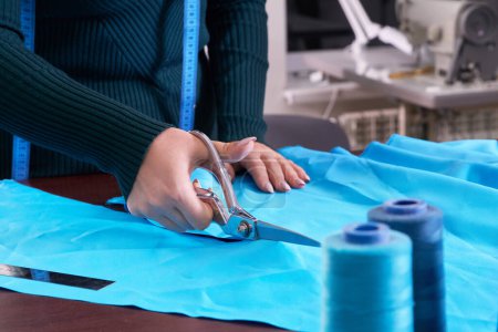 Photo for "Dressmaker cutting blue fabric in tailor studio, atelier shop" - Royalty Free Image