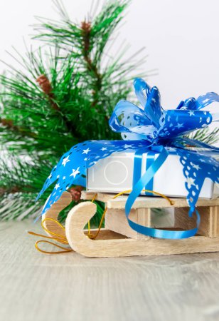 Photo for "A Christmas gift with a large blue bow is lying on a wooden sleigh. Happy New year and merry Christmas. " - Royalty Free Image