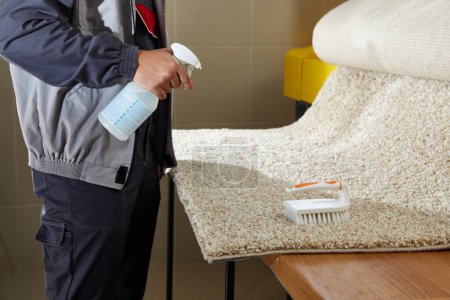 Foto de Detergente de pulverización de hombre en alfombra gris para eliminar manchas en el servicio de limpieza profesional - Imagen libre de derechos