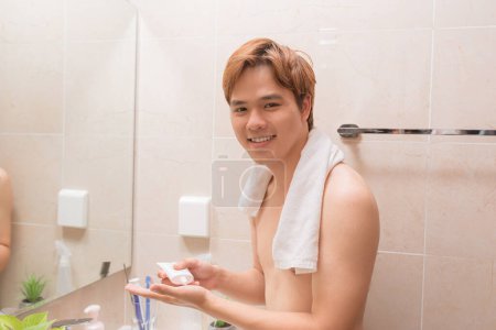 Téléchargez les photos : Portrait de beau sourire gars en bonne santé appliquant de la mousse pour le lavage sur son visage. - en image libre de droit