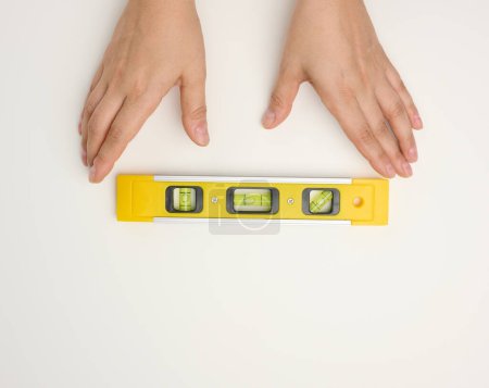 Foto de Manos femeninas sostiene un nivel de construcción de plástico amarillo sobre un fondo blanco - Imagen libre de derechos