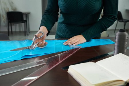 Photo for Dressmaker cutting blue fabric in tailor studio, atelier shop - Royalty Free Image