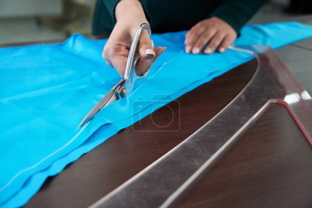 Téléchargez les photos : Dressmaker découpe tissu bleu en atelier tailleur, atelier boutique - en image libre de droit