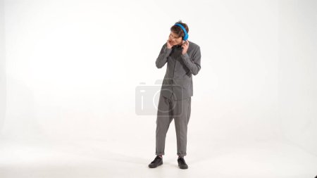 Photo for "Full length dancing young man in grey sports outfit listening music wearing blue wireless headphones. Funny dancing young guy listen to his favourite track or song. 4K footage" - Royalty Free Image