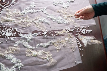Photo for Close-up of female hands of tailor sewing wedding dress using beads and lace in the studio - Royalty Free Image
