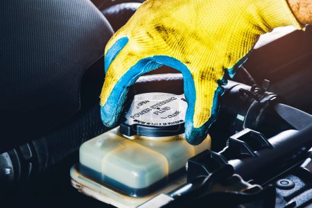 Téléchargez les photos : The mechanic hand is open or close the cap of the power steering fluid to check the hydraulic fluid level - en image libre de droit