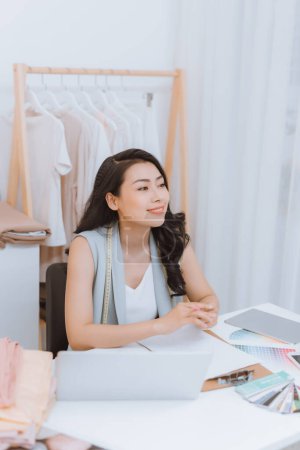 Téléchargez les photos : Portrait de la jeune créatrice de mode asiatique assise au bureau devant son ordinateur portable dans l'atelier - en image libre de droit