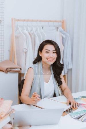 Foto de Una joven diseñadora de moda asiática en su taller trabajando con un portátil - Imagen libre de derechos