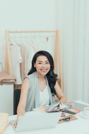 Foto de Retrato de hermosa diseñadora de moda asiática sentada en la oficina / taller - Imagen libre de derechos