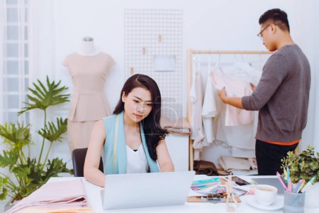 Foto de "Diseñadores de moda en el trabajo. Guapo diseñador masculino elegir el diseño, mientras que su colega que trabaja con el ordenador portátil
." - Imagen libre de derechos