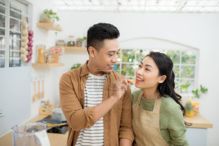 Photo for "Beautiful happy asian couple are feeding each other in the kitchen." - Royalty Free Image