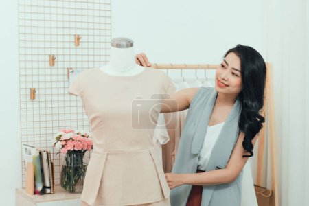 Téléchargez les photos : "Une asiatique travaille dans le studio de l'atelier. Elle s'adapte à la robe sur le mannequin
." - en image libre de droit