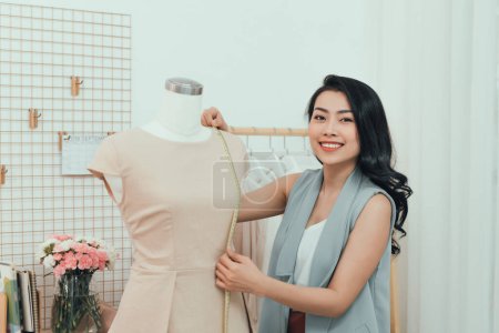 Téléchargez les photos : Une asiatique travaille dans le studio de l'atelier. Elle s'adapte à la robe sur le mannequin - en image libre de droit