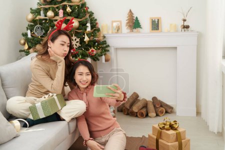 Téléchargez les photos : Mignonnes filles de Noël montrant des cadeaux aux amis de téléphone portable. - en image libre de droit
