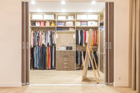 Photo for "Modern wooden wardrobe with clothes hanging on rail in walk in closet" - Royalty Free Image