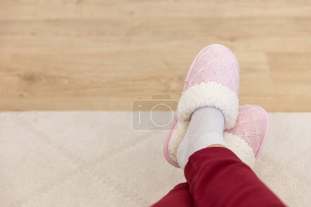 Photo for "Crossed legs wearing pink knitted slippers" - Royalty Free Image