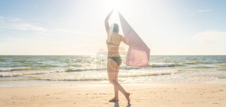 Téléchargez les photos : "Femme debout avec serviette sur la plage avec océan sur fond
" - en image libre de droit