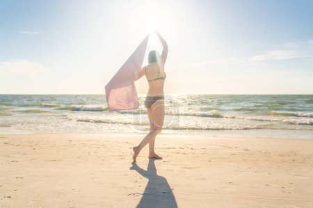 Photo for Woman standing with towel on the beach with ocean on background - Royalty Free Image