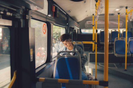 Photo for Young man sitting in city bus and reading a book. - Royalty Free Image