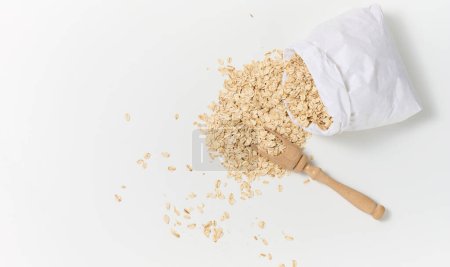 Photo for "raw oatmeal in a white paper bag and a wooden spoon on a white table, breakfast porridge" - Royalty Free Image