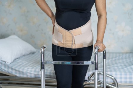 Photo for "Asian lady patient wearing back pain support belt for orthopedic lumbar with walker." - Royalty Free Image