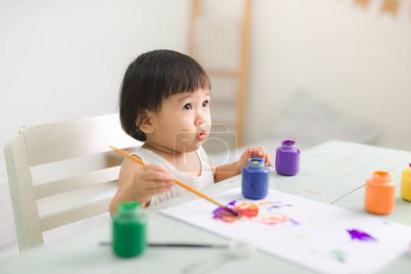Foto de "Divertido riendo asiática bebé niña dibujo con coloridos lápices en casa
" - Imagen libre de derechos
