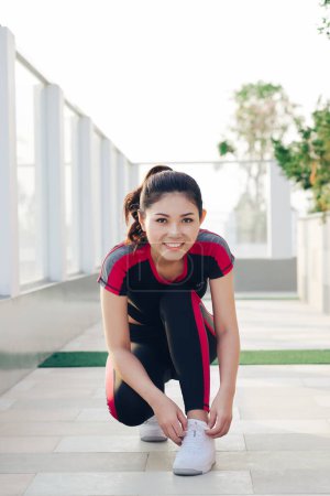Photo for "Young beautiful and attractive sport runner woman tying her shoe sneaker laces smiling happy ready for running and jogging workout at park." - Royalty Free Image