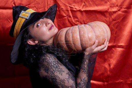 Téléchargez les photos : "Dame d'Halloween portant une tasse de sorcière et tenant une grande citrouille d'Halloween" - en image libre de droit