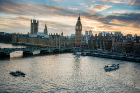 Photo for "London, UK skyline view at sunset with famous landmarks, Big Ben, Houses of Parliament and ships on River Thames with beautiful blue and yellow sky." - Royalty Free Image